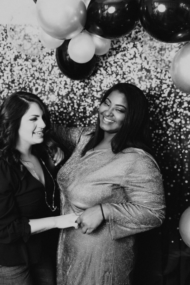 Two guests smiling in front of a sparkle backdrop with balloons